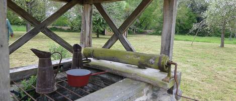 A rustic outdoor structure with a wooden roof, a metal barrel, and a red pot.