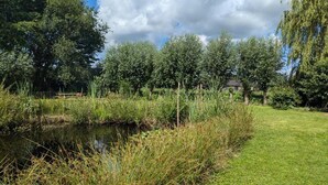 A serene outdoor area with a pond, lush greenery, and a small structure in the background. - Relaxing Woodland Retreat (Rheezerveen)