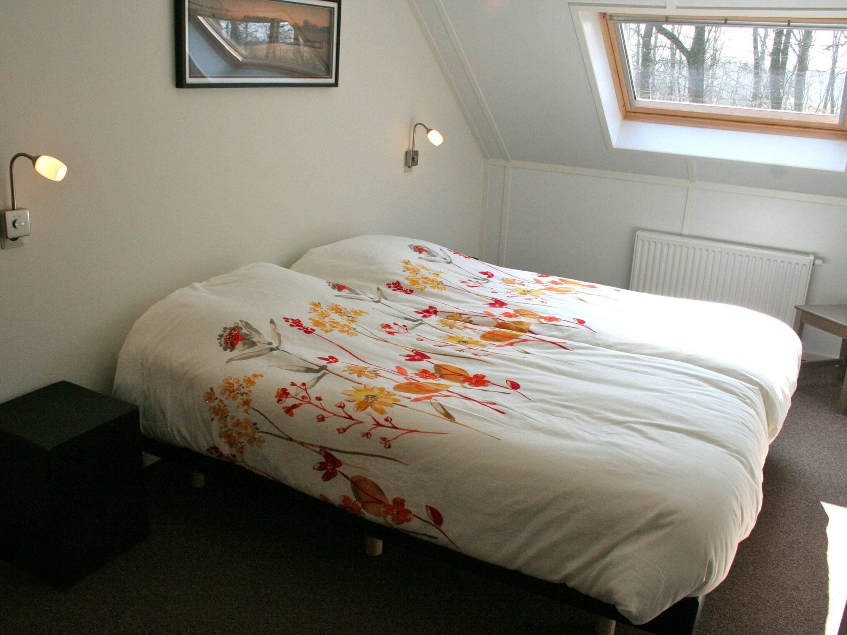 Une chambre à coucher comprenant un lit, une table de chevet, un tableau encadré, une fenêtre et un luminaire fixé au mur.