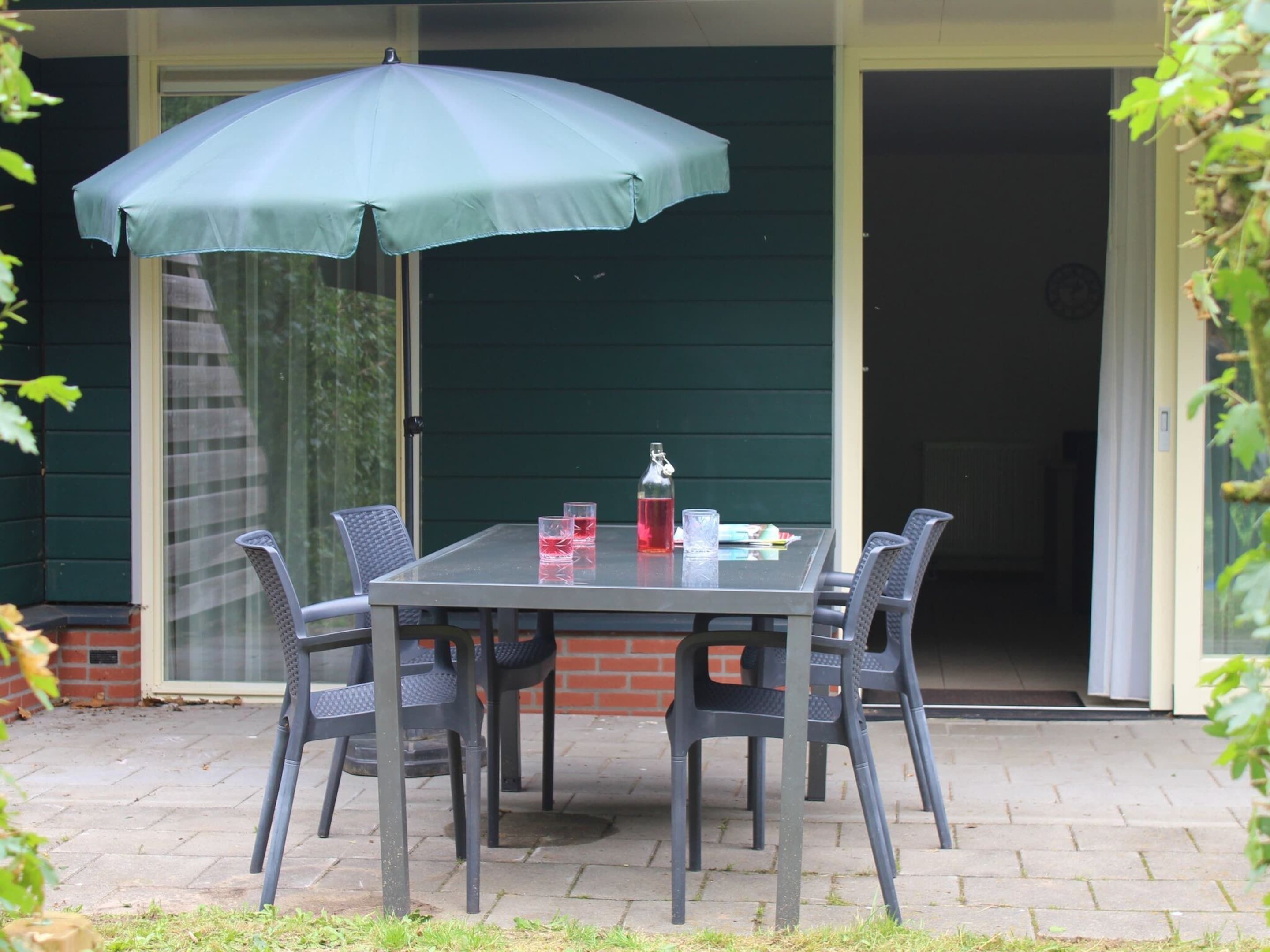 A patio with a table and chairs, an umbrella, and a bottle of water.