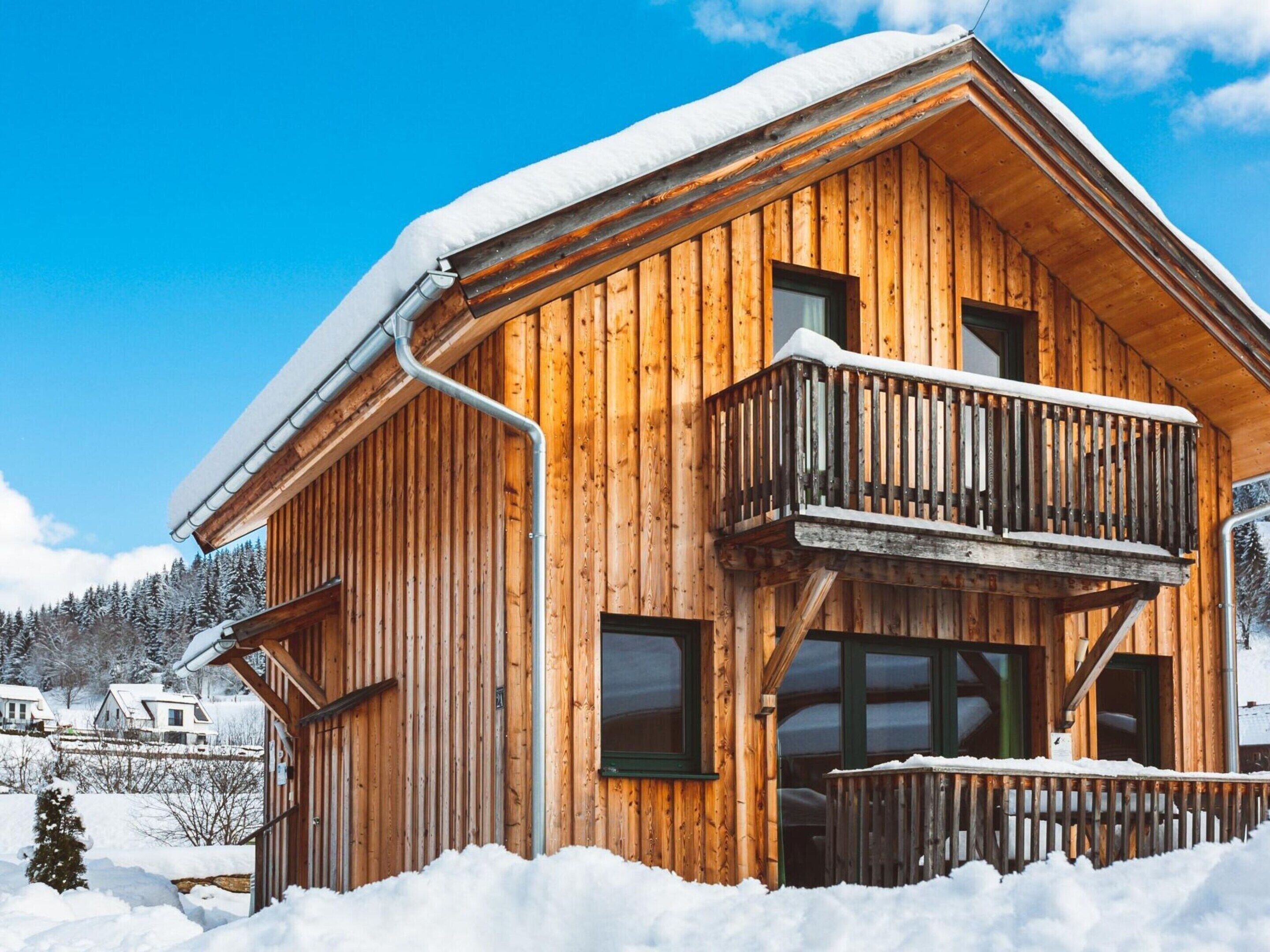 Een houten chalet met balkon, omgeven door sneeuw.