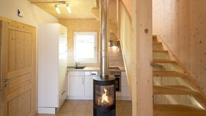 A modern kitchen with a wood-burning stove, white cabinetry, and a wooden staircase.
