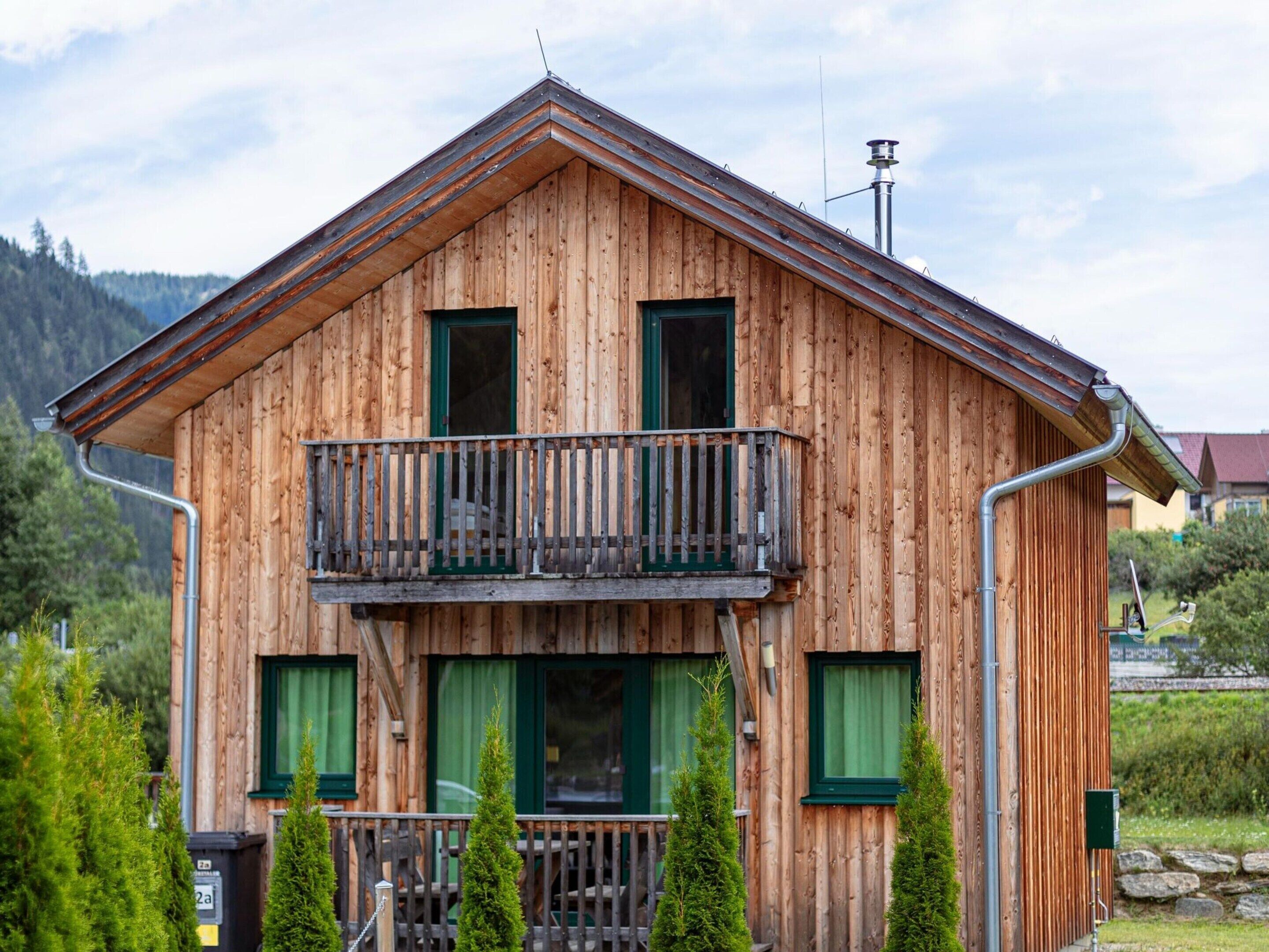 A wooden chalet with a balcony, green shutters, and a metal roof gutter.