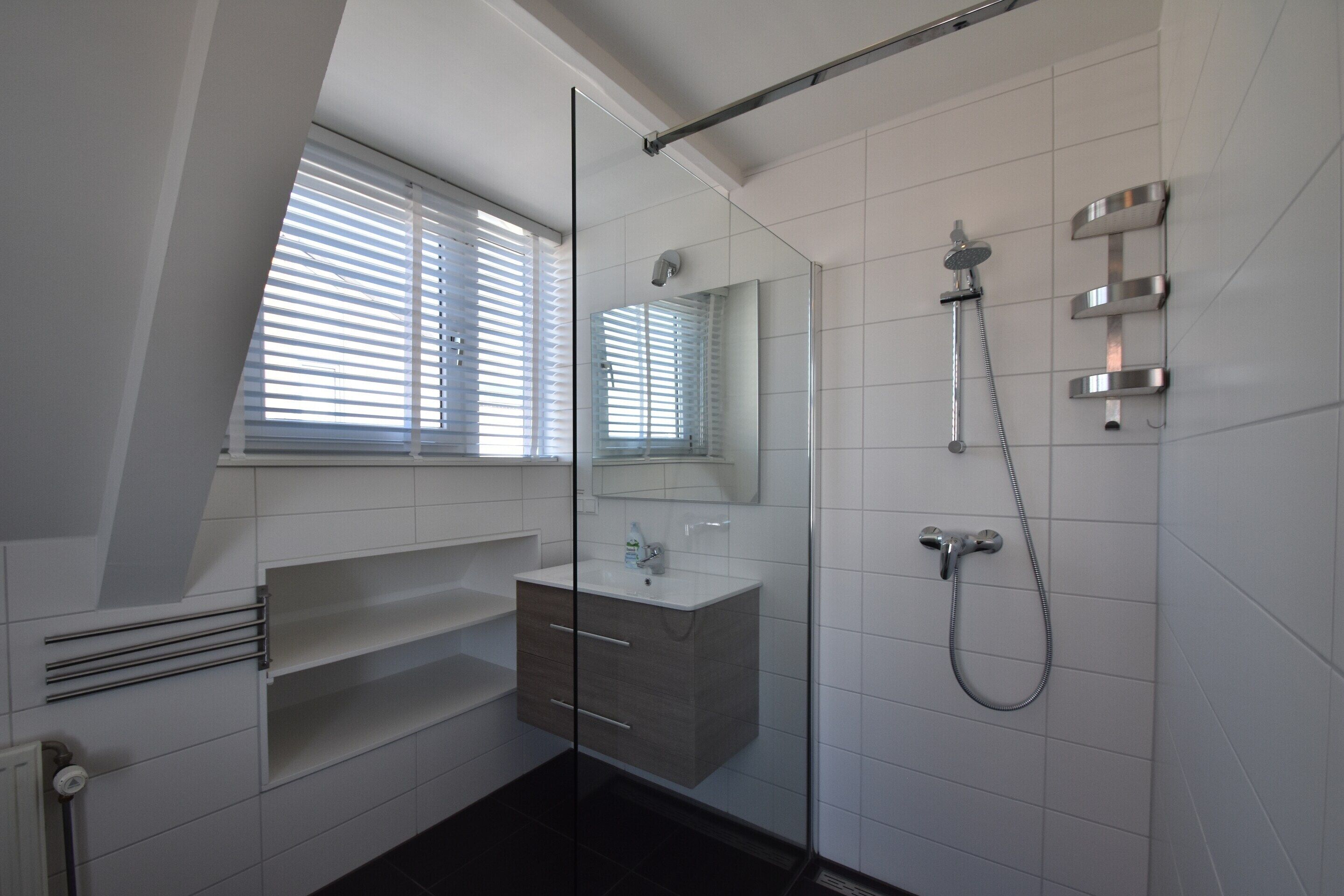 A modern bathroom with a glass shower enclosure, a vanity with a mirror, and a window with blinds.