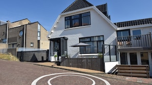 Ein modernes, zweistöckiges Haus mit weißer Fassade und schwarzem Dach, sowie einer kreisförmigen Auffahrt.