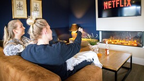 Un salon avec une cheminée, un logo Netflix et deux tableaux encadrés accrochés au mur.