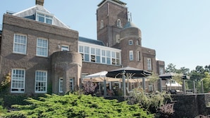A large brick building with multiple windows and a tower. There are outdoor umbrellas and seating areas.
