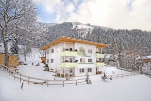 Ein mehrstöckiges Gebäude mit einer grün-weißen Fassade, umgeben von schneebedeckten Bäumen und einer Bergkulisse.