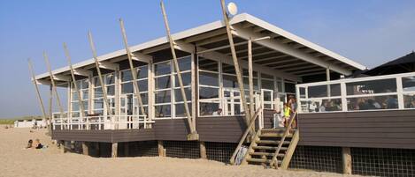 A beachside building with a sloped roof, large windows, and wooden supports.