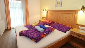 A hotel room with a wooden headboard, two bedside tables with lamps, a bed with purple and orange patterned bedding, and a window with sheer curtains.
