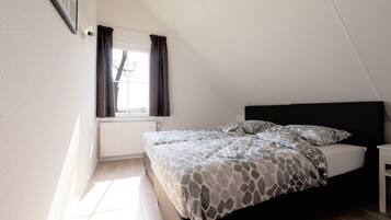 A bedroom with a bed, a window with curtains, a radiator, and a wall-mounted picture.