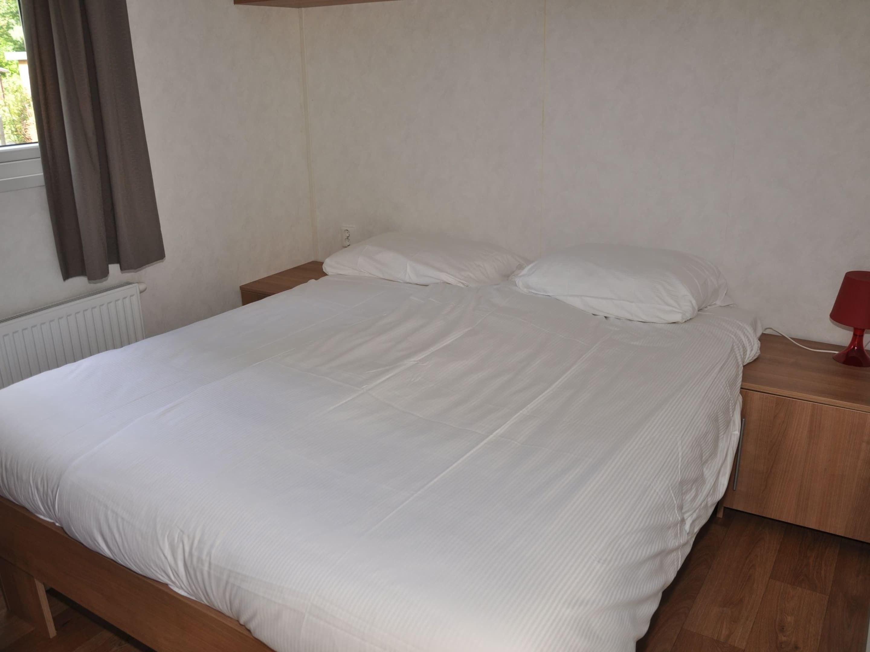 A single bed with white bedding in a room with a wooden floor and a white wall.