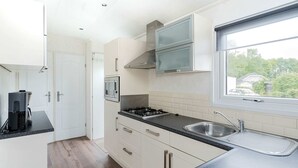 A modern kitchen with white cabinets, a black countertop, a gas stove, a built-in oven, and a window with a view of greenery. - Chalet in Parc de Kievit With Private Garden (Baarle-Nassau)
