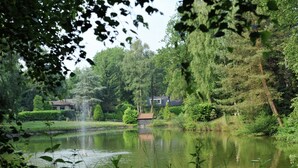 A serene lakeside setting with a house surrounded by lush greenery and trees. - Chalet in Parc de Kievit With Private Garden (Baarle-Nassau)