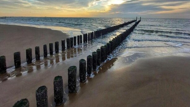 Une plage avec un brise-lames en bois qui s’avance dans la mer, sous un ciel nuageux.