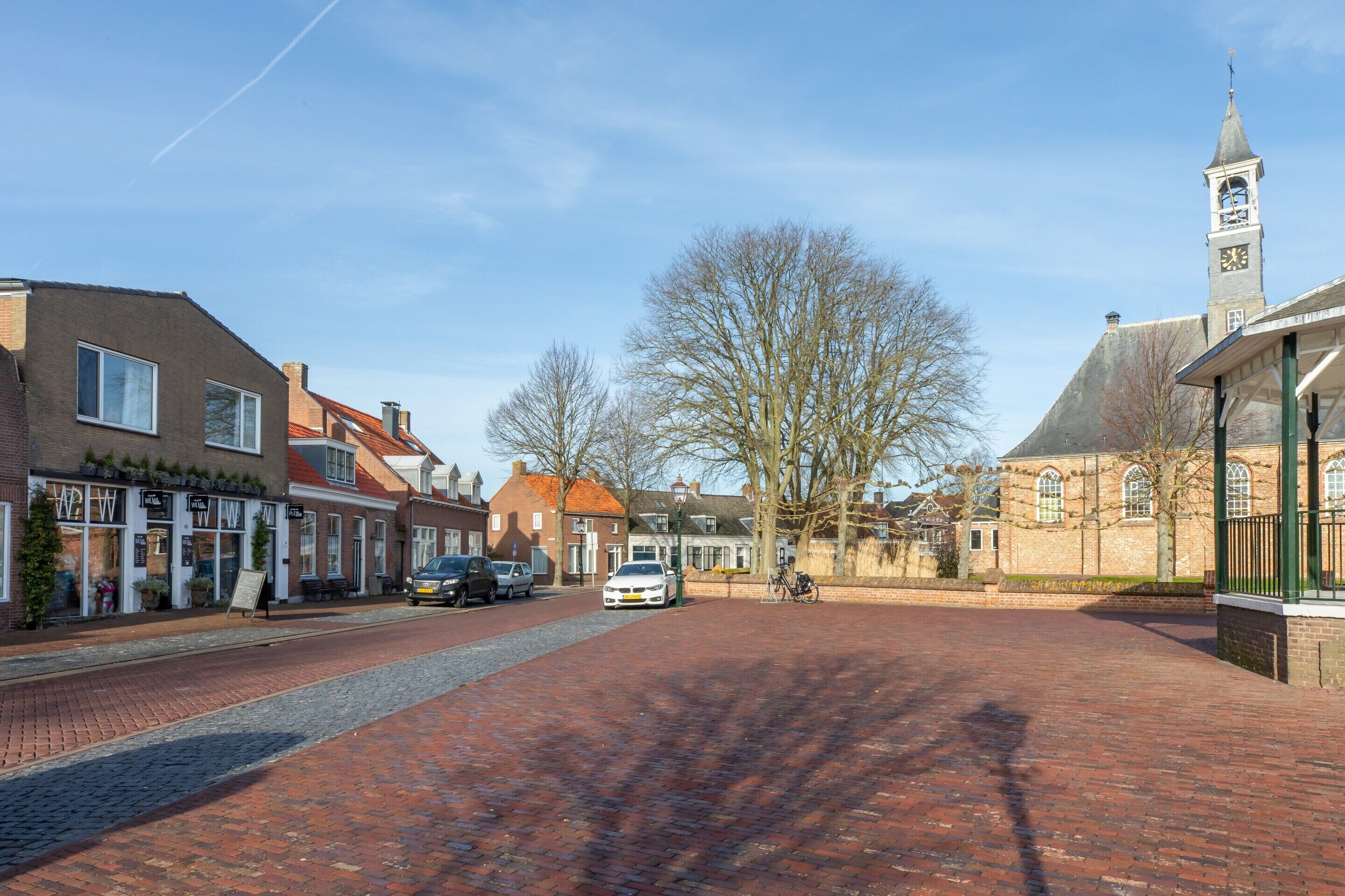 En kullerstensgata med historiska byggnader, en kyrka med ett klocktorn och en klar himmel.