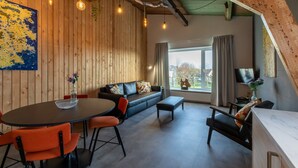 Une pièce chaleureuse avec un mur en bois, un canapé, une table à manger avec des chaises et une grande fenêtre donnant sur un beau paysage.