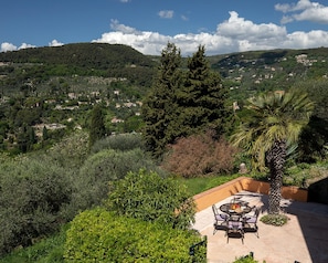 A patio with a table and chairs, surrounded by lush greenery and a view of a hillside village. - 18thc Perfumer's Home, Heated Pool & View (Grasse)