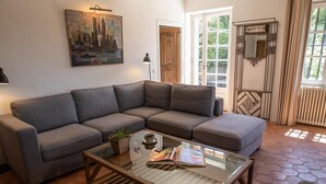 Una sala de estar con un sofá modular, una mesa de centro de vidrio, una planta en maceta y un cuadro con una vista urbana en la pared.