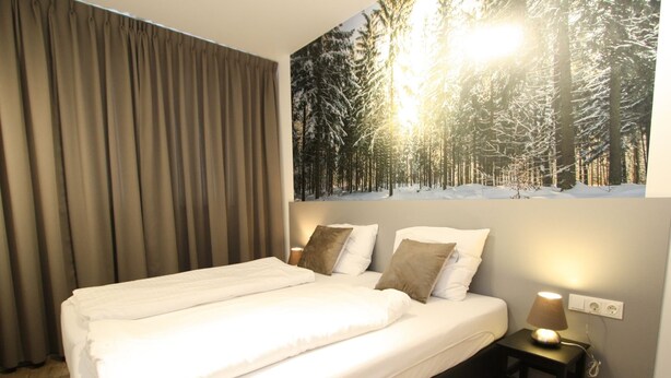 A neatly made bed with white linens and two pillows, a bedside table with a lamp, and a large wall mural of a snowy forest scene. - Vogue Apartment in Sankt Margarethen im Lungau near Ski Lift (Sankt Margarethen im Lungau)