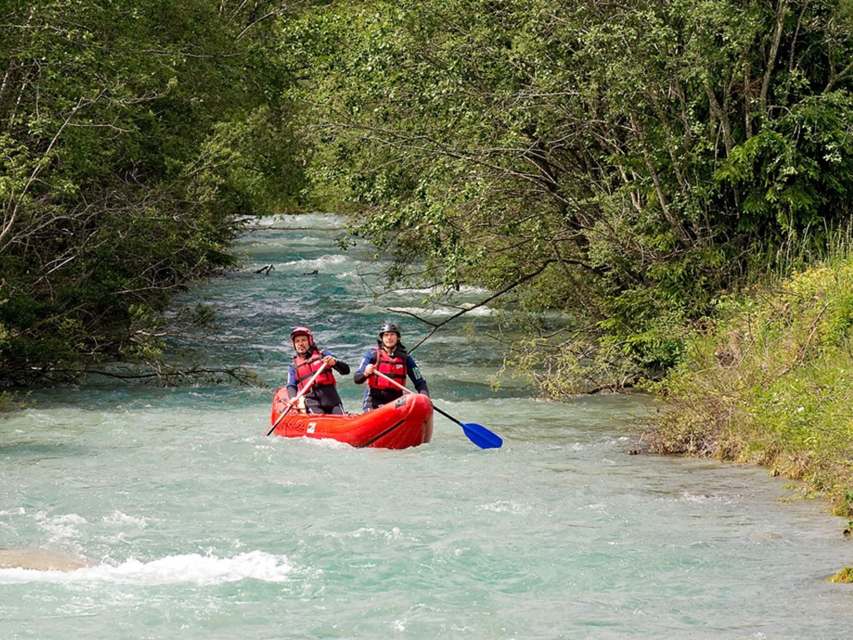 Deux personnes à bord d’un radeau rouge naviguent sur une rivière bordée d’une végétation luxuriante.