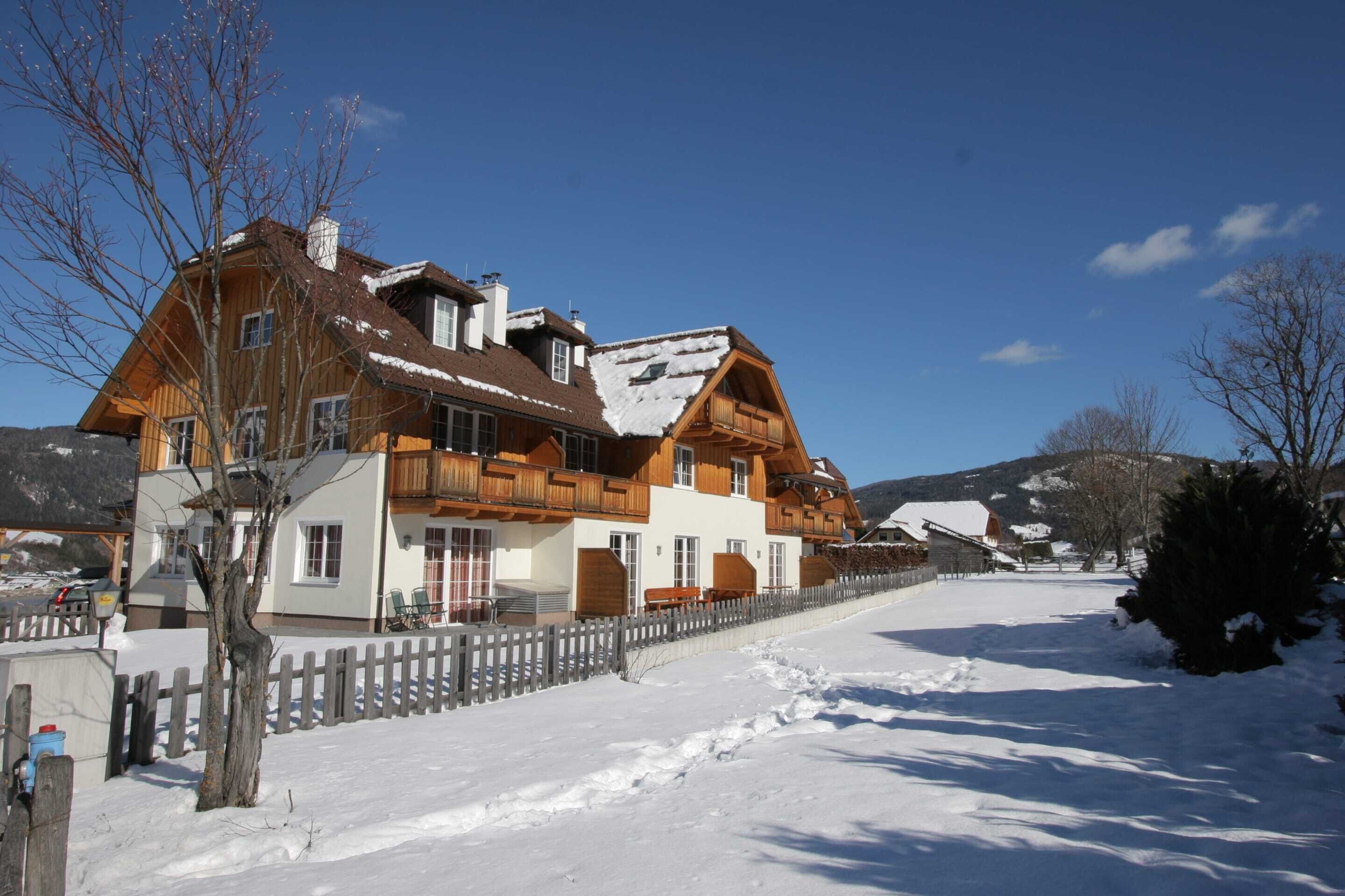 A large wooden chalet with multiple balconies, a snow-covered roof, and a white facade.
