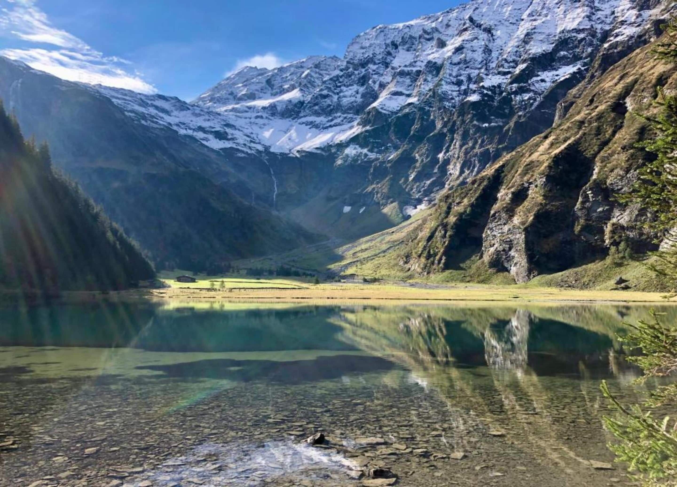 Ein klarer Bergsee mit Spiegelungen, umgeben von zerklüfteten Bergen und viel Grün.