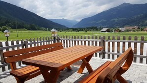 A wooden bench and picnic table set on a paved patio with a view of green fields and mountains. - Vogue Apartment in Sankt Margarethen im Lungau near Ski Lift (Sankt Margarethen im Lungau)