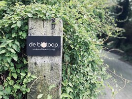 A wooden post with a black sign that reads "de biotoop" and "vakantiewoning".