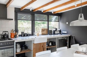 A modern kitchen with a large window, wooden beams, and a white dining area.