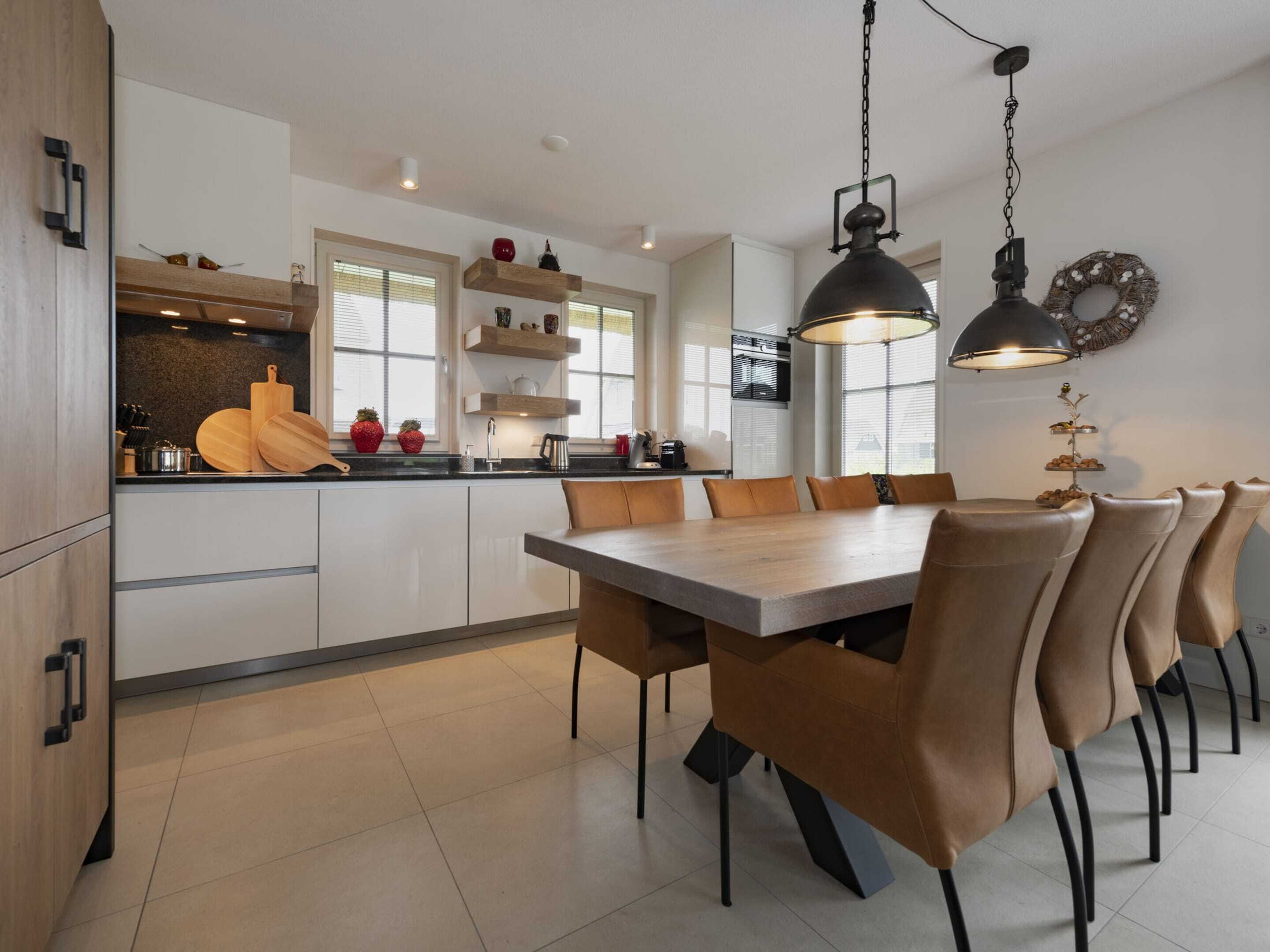 Una cucina moderna con mobili bianchi, un'isola centrale e un'area pranzo con un tavolo grande e sedie.