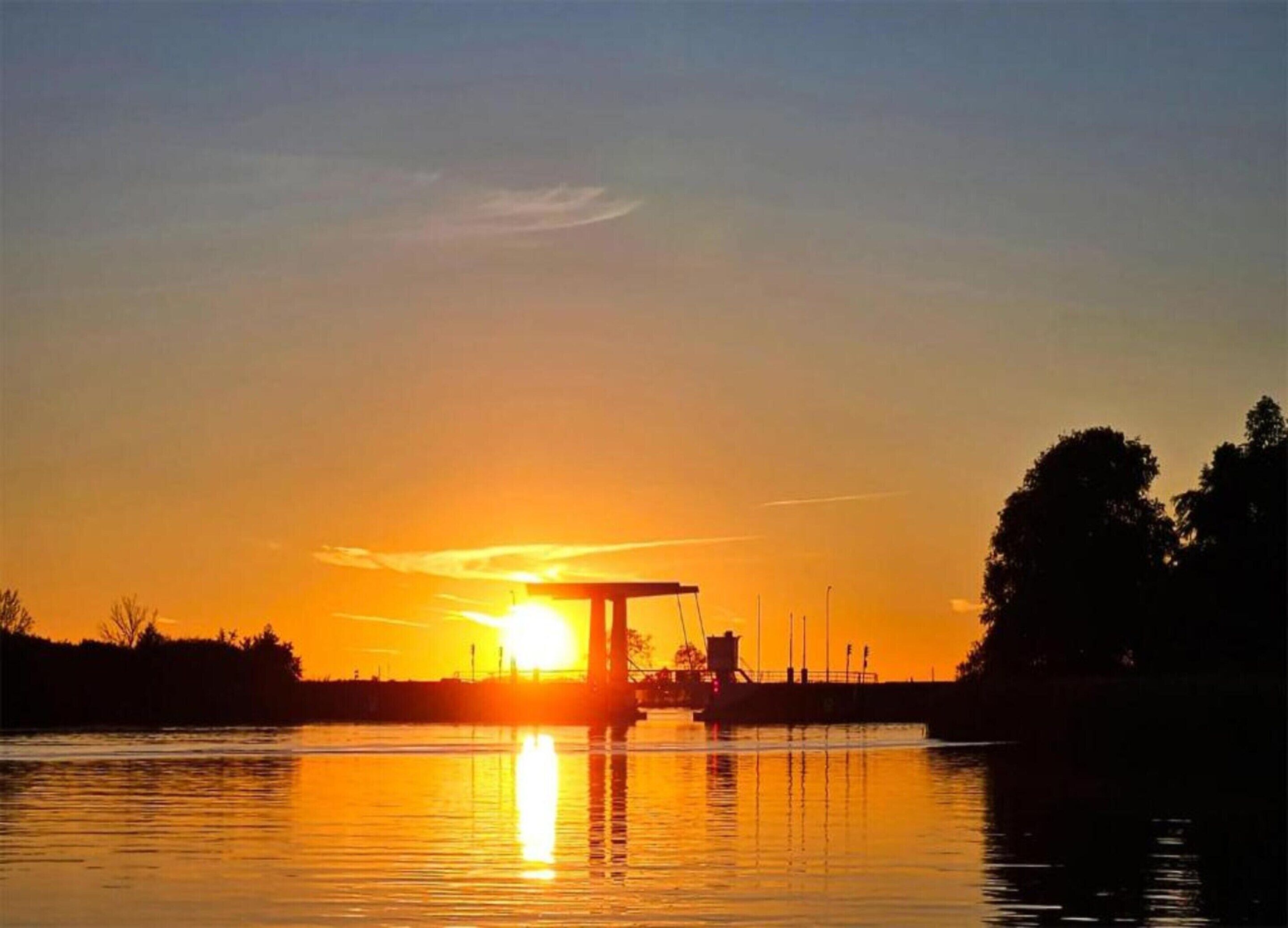 Un coucher de soleil sur une étendue d’eau calme, avec un quai et un bateau.