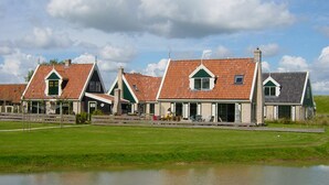 Una hilera de casas tradicionales con tejados a dos aguas y chimeneas, un área verde al frente y una masa de agua.