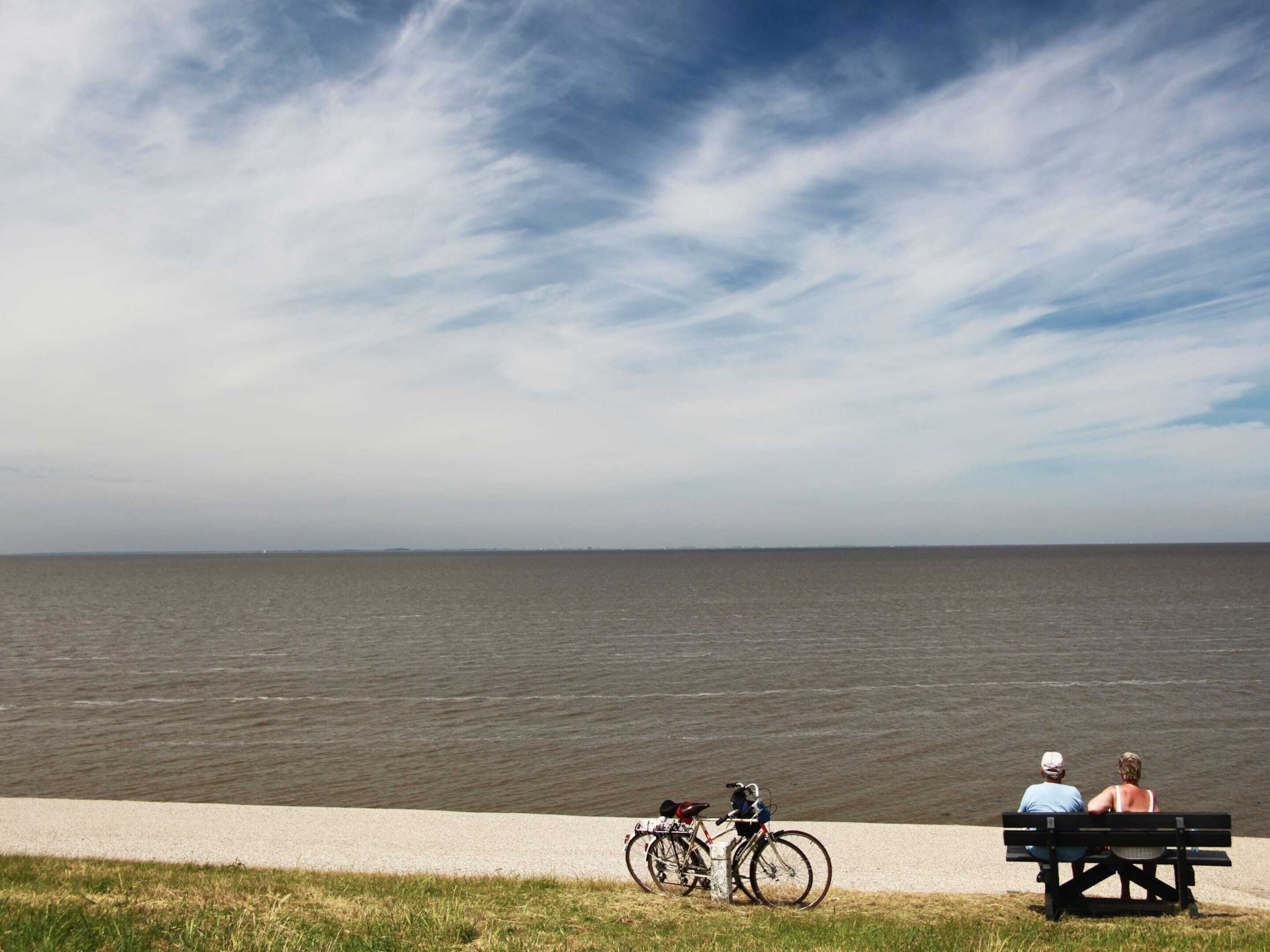 A bench by a lake with bicycles parked nearby.