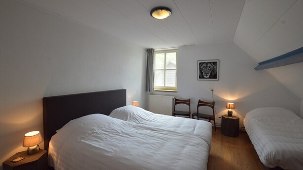 Une chambre avec deux lits, une fenêtre, un radiateur et un tableau encadré au mur.