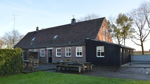 Une maison à deux étages, avec une façade en briques, un toit en pente et un petit jardin à l’avant, agrémenté d’un banc et d’une table.