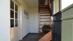 Un couloir étroit avec un escalier en bois, un radiateur et une porte dotée de panneaux en verre dépoli.
