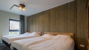 Une chambre avec deux lits, des murs lambrissés, un ventilateur de plafond et une fenêtre avec des rideaux.