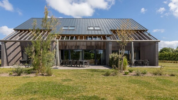 Une maison moderne avec un toit en pente, de grandes fenêtres et un espace patio.