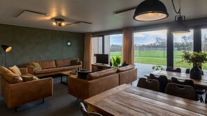 Un salon moderne avec un grand canapé, une table à manger et un téléviseur. Une grande fenêtre offre une vue sur un champ verdoyant.