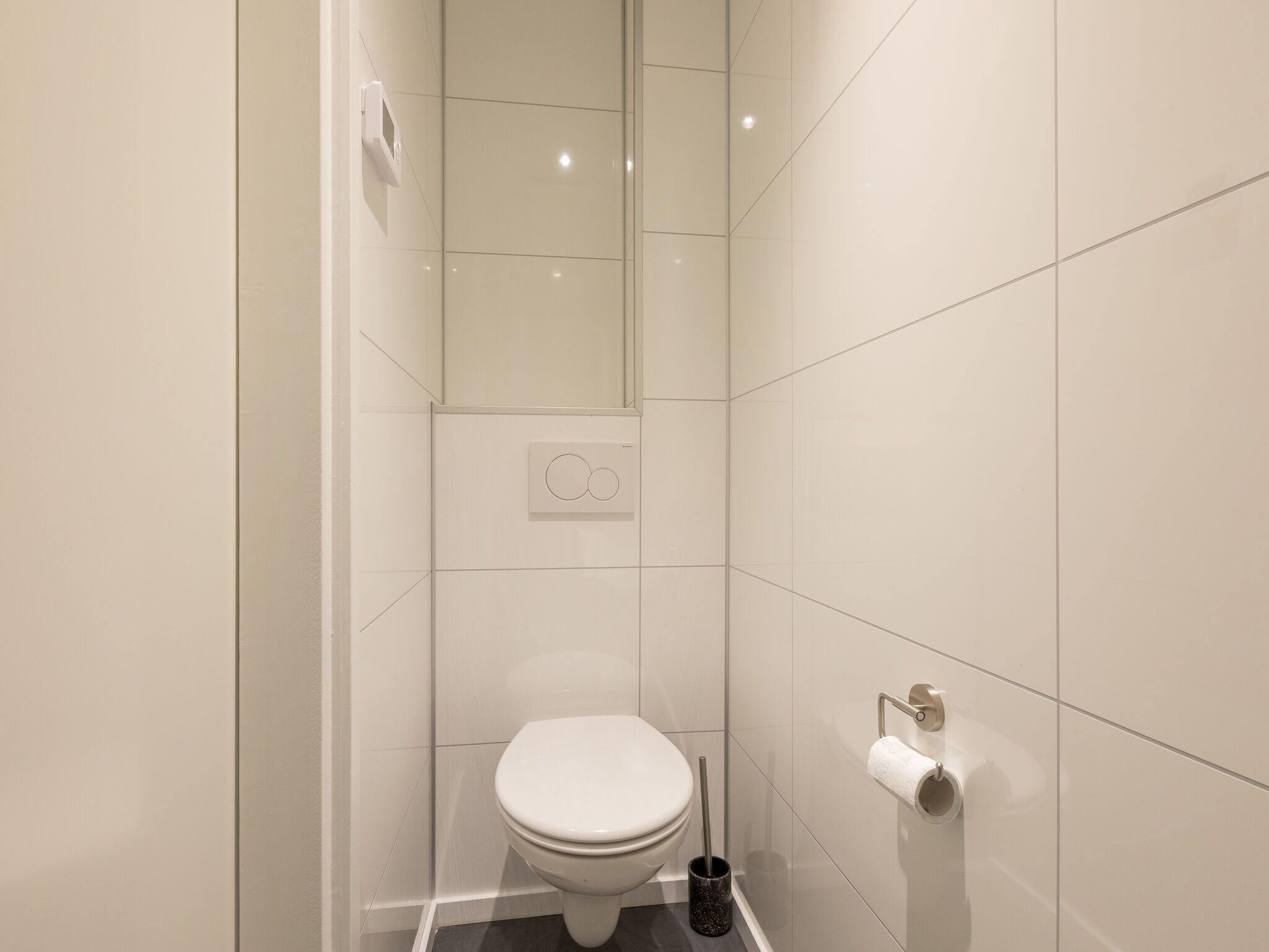 A modern bathroom with a toilet, a hand dryer, and a toilet paper holder.