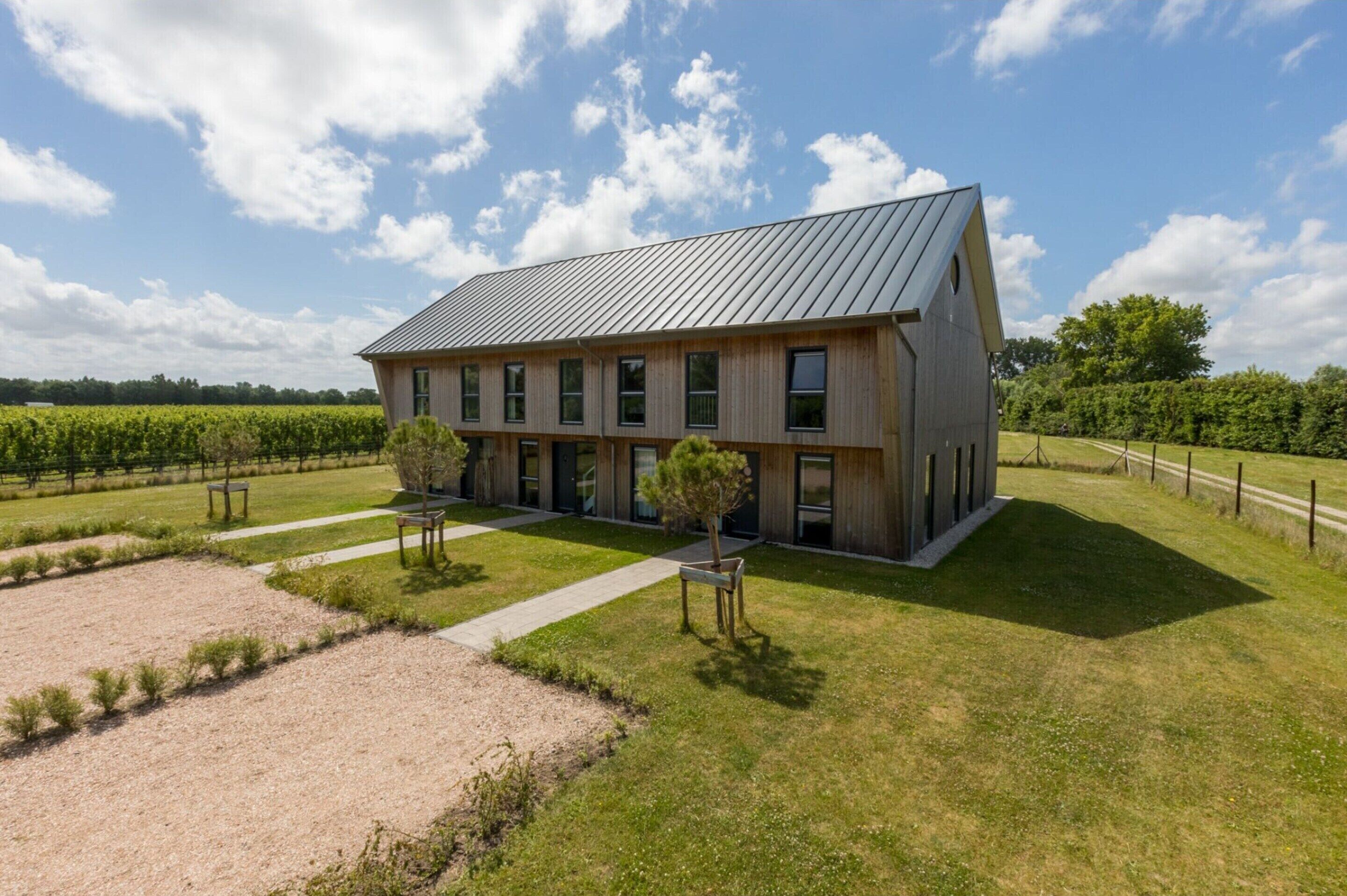 Un bâtiment moderne doté d’un toit en pente, de grandes fenêtres et d’une pelouse verdoyante agrémentée de sentiers.