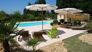 Zona de piscina con sillones de descanso, sombrillas y un edificio al fondo.