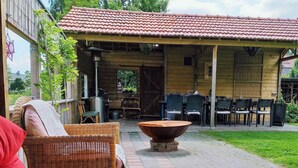 An outdoor patio with wicker furniture, a fire pit, and a covered wooden structure with a tiled roof. - Holiday Home in Soerendonk With Garden (Soerendonk)