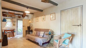 A cozy room with a bed, a wicker chair, a table with a lamp, and framed botanical prints on the wall. - Cottage in Oppede With Pool and Garden (Oppede)