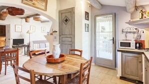 A cozy kitchen with a dining table, chairs, a microwave, and a door with a lace curtain. - Cottage in Oppede With Pool and Garden (Oppede)