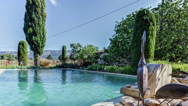 A swimming pool with clear water, surrounded by large rocks and greenery. - Cottage in Oppede With Pool and Garden (Oppede)