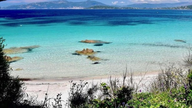 A beach with clear turquoise water, rocky outcrops, and distant mountains. - Wheelchair-friendly Escape (Varsberg)