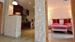A room with a stone wall, a bed with red bedding, a washing machine, and a kitchen area. - Wheelchair-friendly Escape (Varsberg)