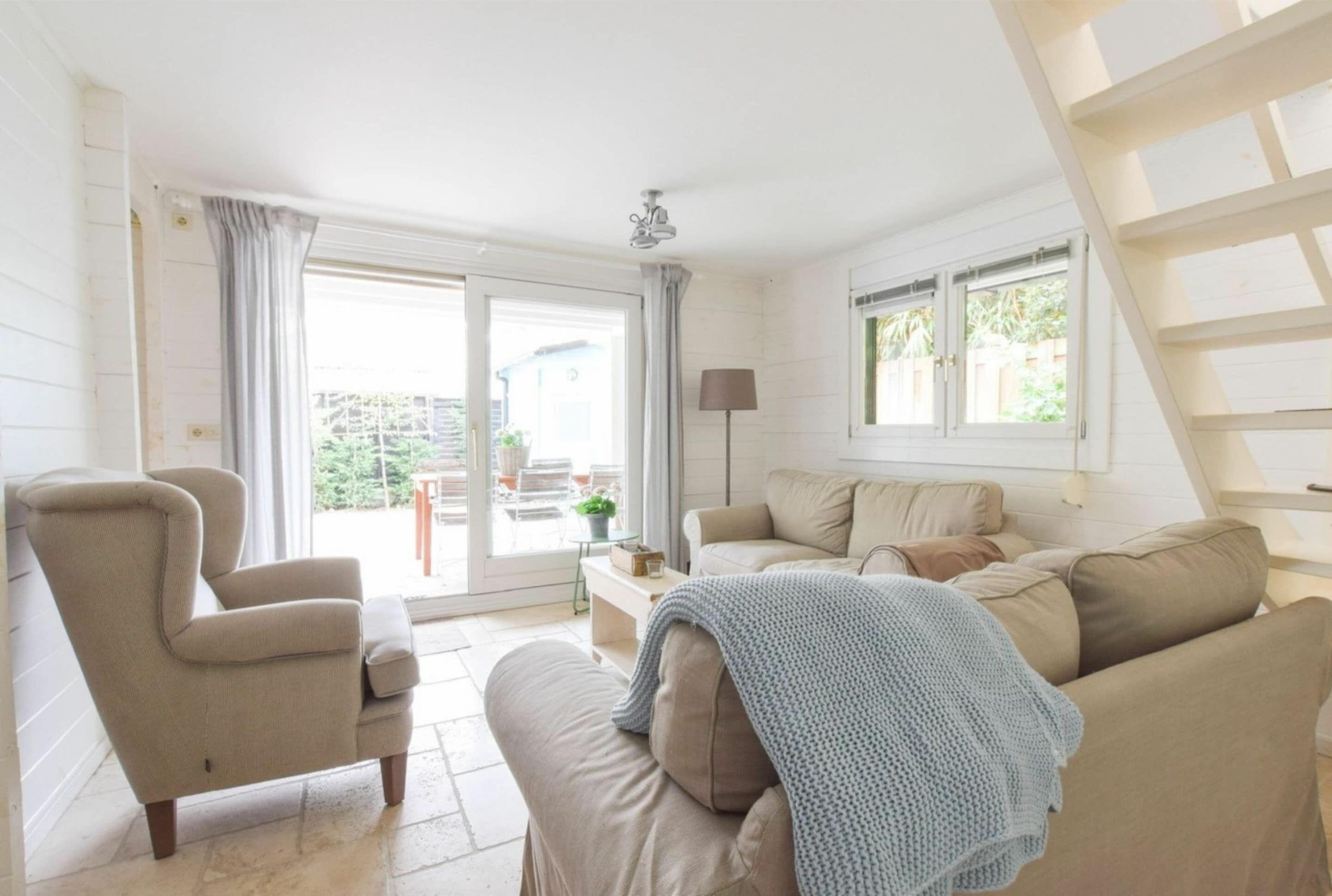 Amplia sala de estar con sofá, sillón y una pequeña mesa. Se ve una ventana con cortinas y vistas al exterior.